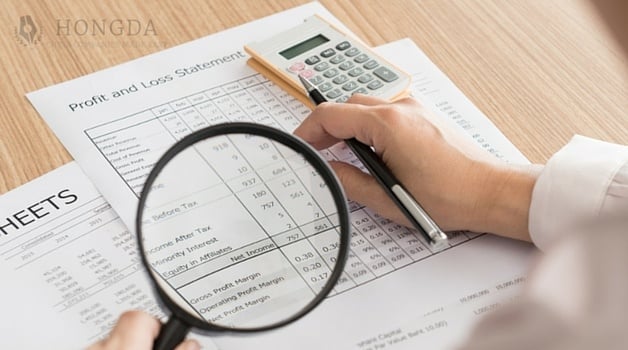 someone using magnifying glass looking at audits while holding a pen