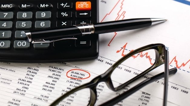 calculator, pen and glasses on top of financial papers