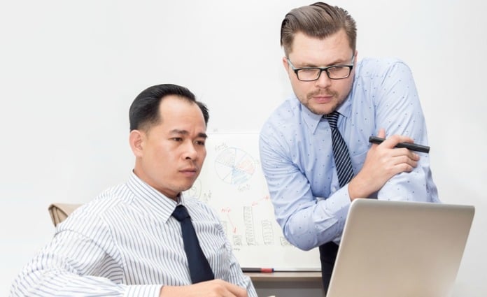 Two office workers looking at laptop screen with puzzled expressions.