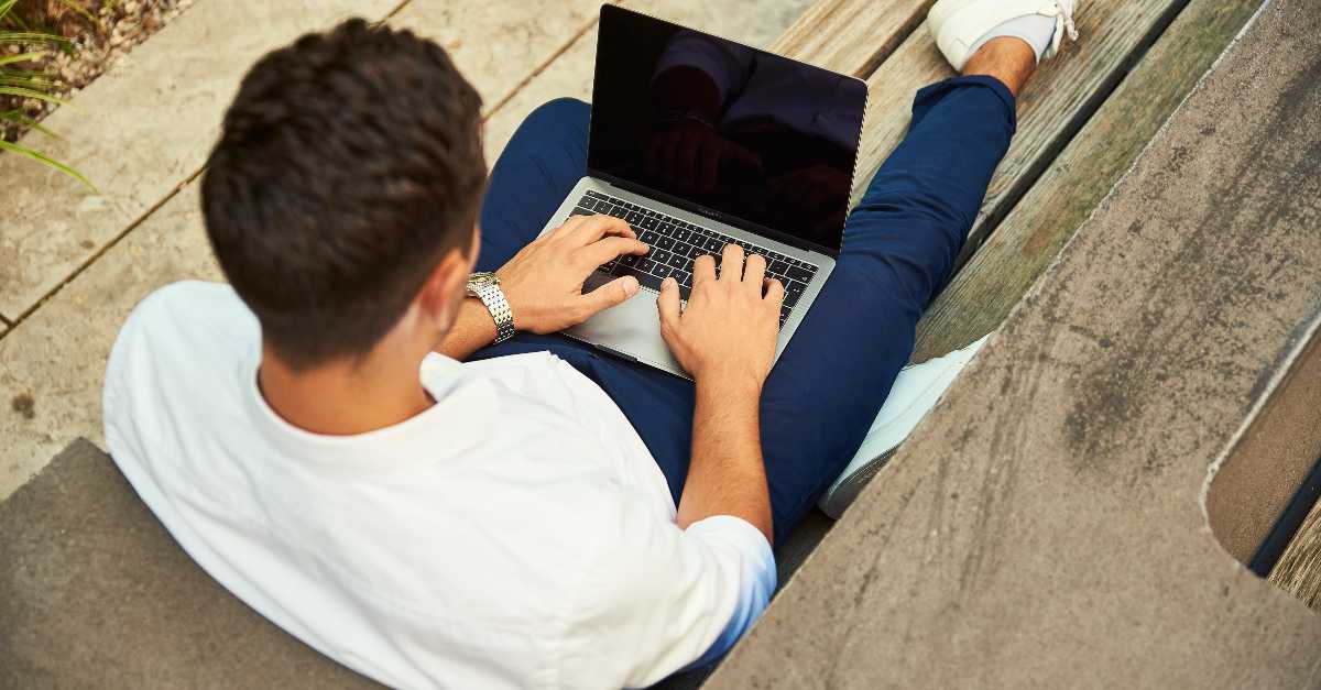 Male casually sitting on the ground typing on laptop